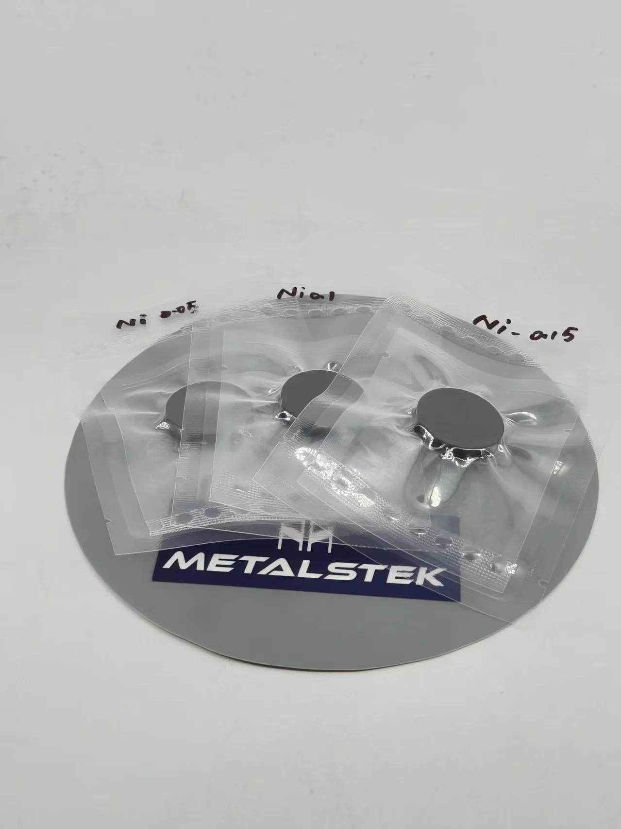 Three dark circular targets in individual transparent pouches, photographed together above a MetalsTek nameplate.