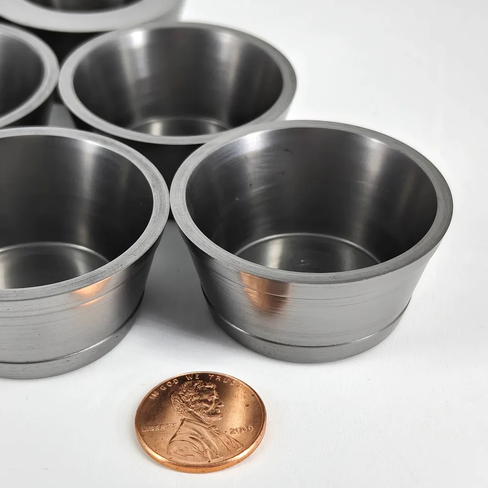 Close-up of machined graphite crucibles beside a coin for visual scale
