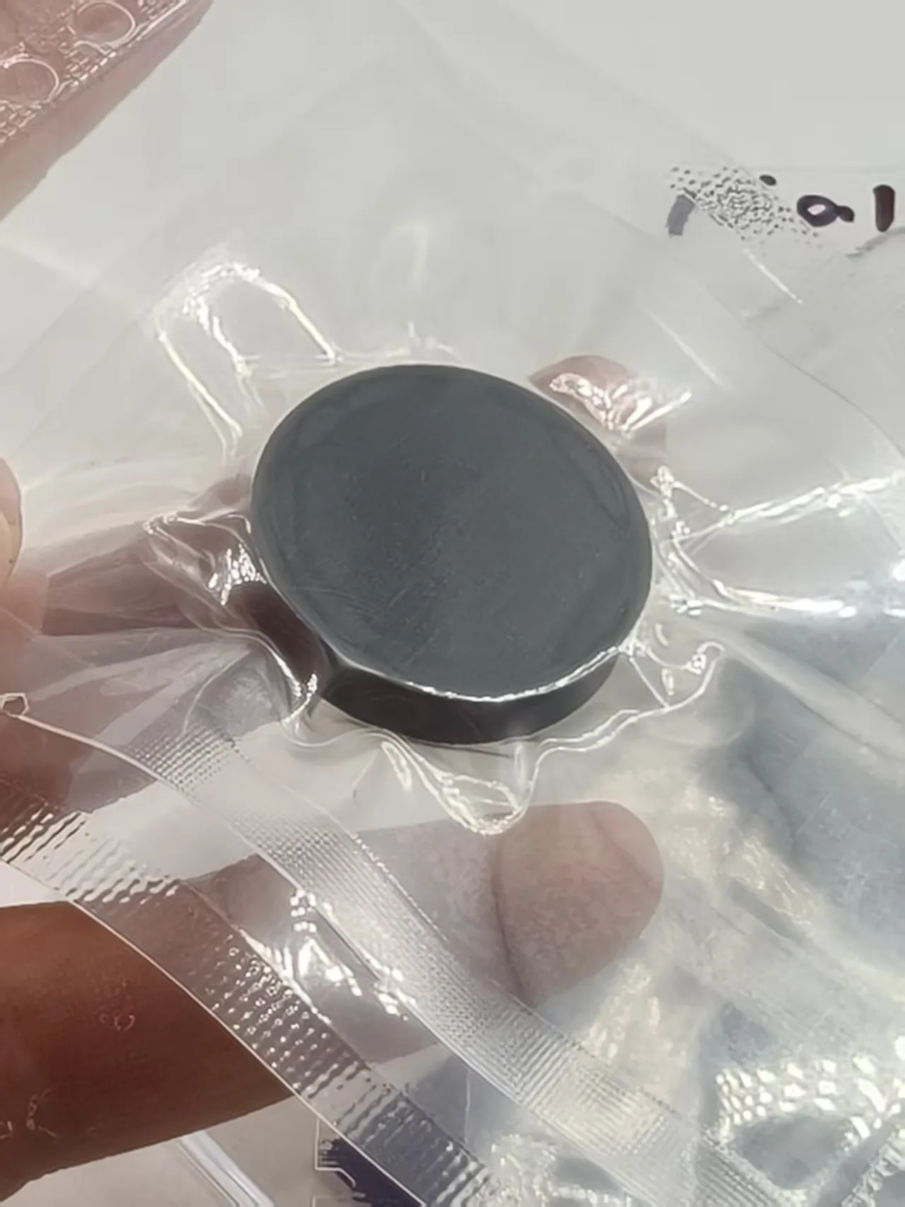 Close-up of a dark circular target held inside a transparent pouch, with its face and edge visible through the packaging.